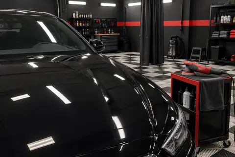 Capô de carro preto e politriz em uma bancada de detalhamento